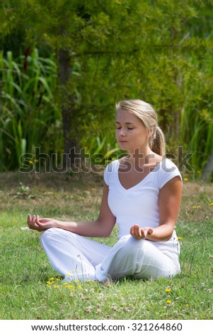 outdoors meditation - focused young yoga woman exercising in lotus pose,closing eyes to focus on inner peace to relax and meditate on grass with green bushy background
