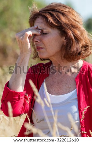 Hay fever allergies - beautiful middle age woman with sinus pain massaging her face for relaxation in dry meadow,natural summer daylight