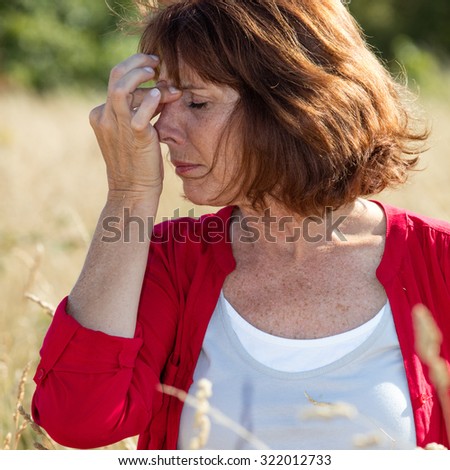 Hay fever allergies - beautiful aging woman with sinus pain massaging her nose against headache in dry meadow,natural summer daylight