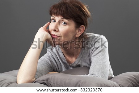 satisfaction and smile concept - thinking 50s woman leaning on her hand and elbow,lying down on bed cushions for happiness and comfort