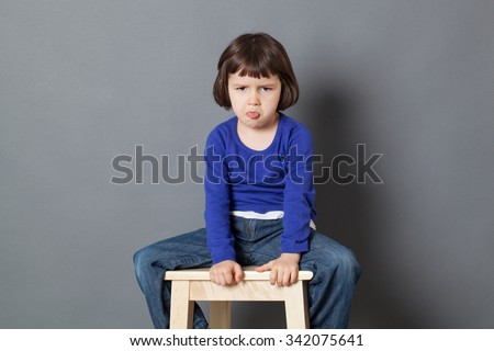 kid attitude concept - sulking 4-year old child sitting on wooden stool sticking tongue for arrogance and bad behavior,studio shot