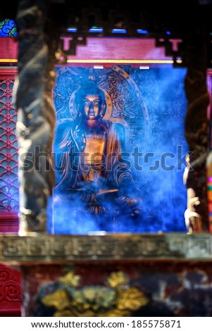 Smoked filled temple with Buddha partially  visible in the background behind a curtain of blue incenses  smoke.