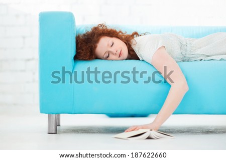 Tired young woman  lying on a sofa  at home with a book