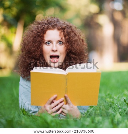Young beautiful woman surprised by the story she is reading in her book.