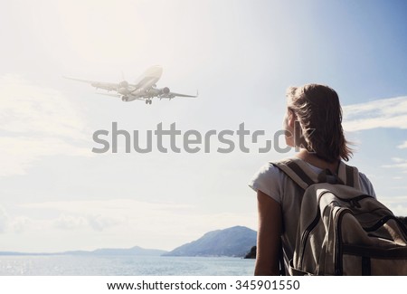 Back side of traveler girl looking at the flying plane above the sea, travel and active lifestyle concept