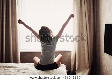 Woman stretching in bed after waking up, back view