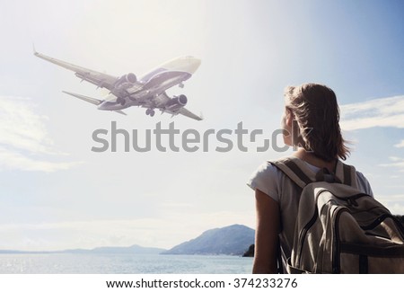 Back side of traveler girl looking at the flying plane above the sea, travel and active lifestyle concept