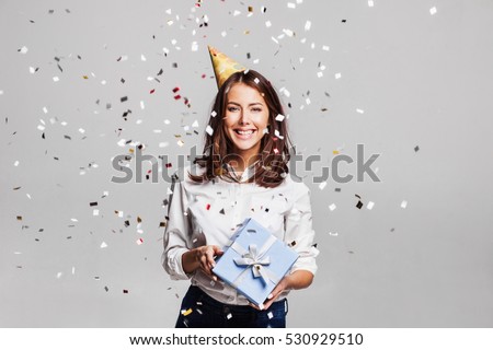 Beautiful happy woman with gift box at celebration party with confetti falling everywhere on her. Birthday or New Year eve celebrating concept