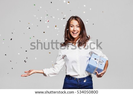 Beautiful happy woman with gift box at celebration party with confetti falling everywhere on her. Birthday or New Year eve celebrating concept
