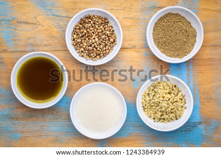 set of hemp seed product:s hearts, protein powder, milk and oil in small white bowls against grunge wood