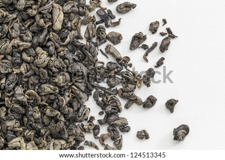 background texture of loose leaf Chinese gunpowder (pearl) green tea spilled over white artist canvas