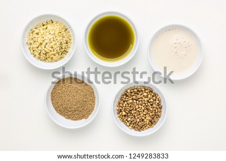 collection of hemp seed products: hearts, protein powder, milk and oil in small white bowls against white art canvas