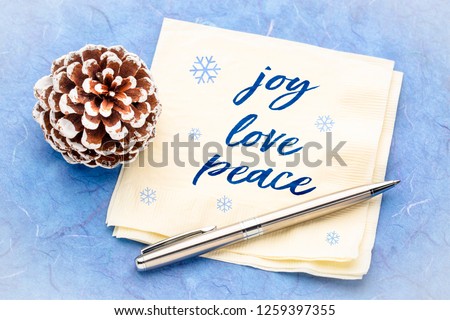 joy, love, peace concept - handwriting on a napkin with pine cone decoration against blue mulberry paper