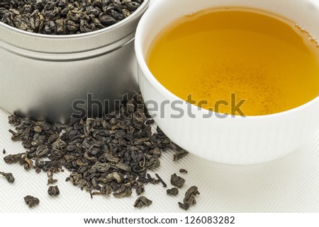 gunpowder green tea - a white cup of drink and loose leaves on canvas