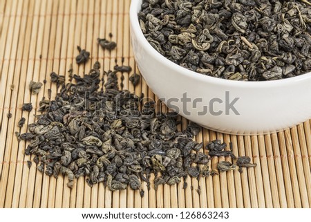loose leaf gunpowder green tea in a white china cup and spilled over bamboo mat