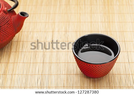Japanese cup of tea with a tetsubin on a bamboo mat - a traditional cast iron red hobnail design with black enamel inside