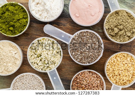 scoops of superfood - healthy seeds and powders (white and brown chia, brown and golden flax, hemp, pomegranate fruit powder, wheatgrass, hemp and whey protein, maca root) - top view