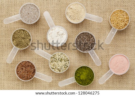 scoops of superfood - healthy seeds and powders (white and black chia, flax, hemp, pomegranate fruit powder, wheatgrass, hemp and whey protein, maca root) on canvas