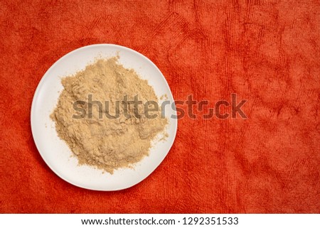 maca root powder on white ceramic plate against red textured paper with a copy space