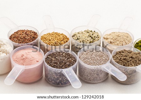 scoops of superfood - healthy seeds and powders (white and black chia, flax, hemp, pomegranate fruit powder, wheatgrass,whey protein, maca root) on white tablecloth