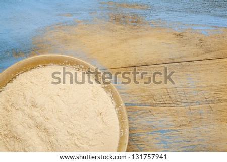 small ceramic bowl of African baobab fruit powder against grunge painted wood background with copy space