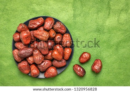 dried jujube fruits on a black plate against textured bark paper