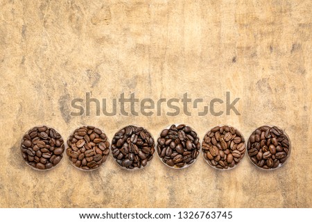 sampler of coffee beans from different parts of the world - overhead view of  round bowls against handmade textured paper with a copy space