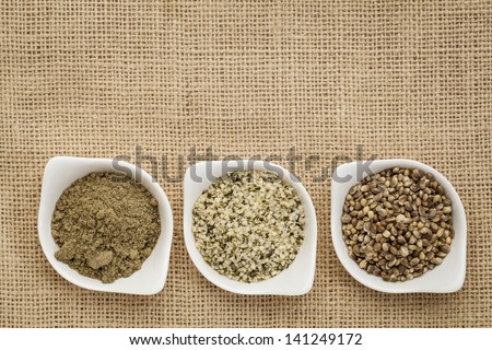 hemp products: seeds, hearts (shelled seeds) and protein powder in small ceramic bowls on burlap canvas