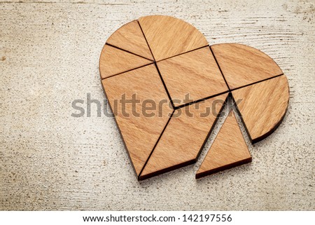 heart version of tangram, a traditional Chinese Puzzle Game made of different wood parts to build abstract figures from them, on white painted barn wood