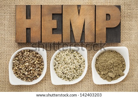 hemp products: seeds, hearts (shelled seeds) and protein powder in small ceramic bowls on burlap canvas with word hemp spelled in letterpress wood type