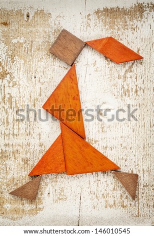 abstract figure of a walking or running girl built from seven tangram wooden pieces, a traditional Chinese puzzle game; rough white painted barn wood background