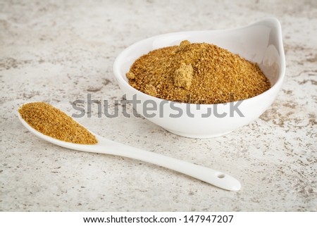 small ceramic bowl of unrefined coconut palm sugar against a ceramic tile background with a spoon