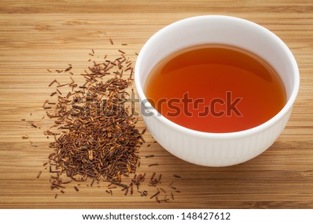 rooibos red tea  -  a white cup of a drink and loose leaves on bamboo wood background, tea made from the South African red bush, naturally caffeine free