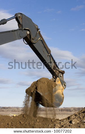 Excavator arm and scoop full of dirt at road construction against blue sky