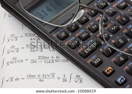 Scientific calculator with pi number on a display and reading glasses against math text book with integral tables. These are real devices, not props, showing some wear and dust.