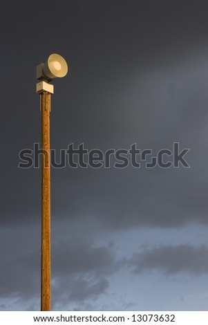high decibel, battery operated,  electromechanical warning siren on a tall post against stormy sky