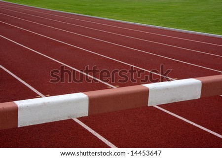steeplechase barrier across red running tracks with white lines and green field in a background