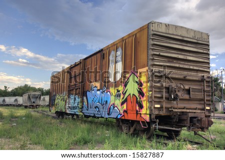 Union Pacific railroad car covered with graffiti on a siding track, hopper cars for grain transport in a background