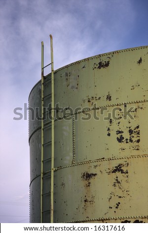 a ladder to the top of an old storage tank or grain bin (metal sheets joined with rivets) against sky