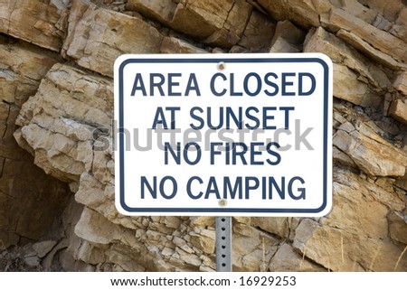 area closed at sunset, no fires or camping - white warning sign in front of climbing rock cliff