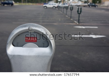 parking meter showing expired time in red, out of focus parked cars in background