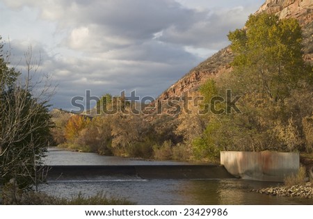 A diversion dam for farmland irrigation on the Cache la Poudre River in foothills of Colorado Rocky Mountains above Fort Collins, late fall scenery with high cliffs and cloudy sky