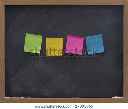 four blank, colorful (green, yellow, red, blue) sticky notes on blackboard with strong eraser smudge patterns