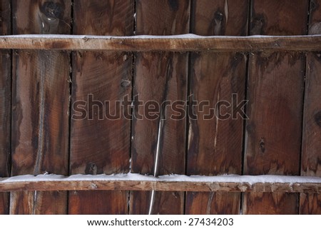 weathered wood of old barn wall with gaps between planks and snow