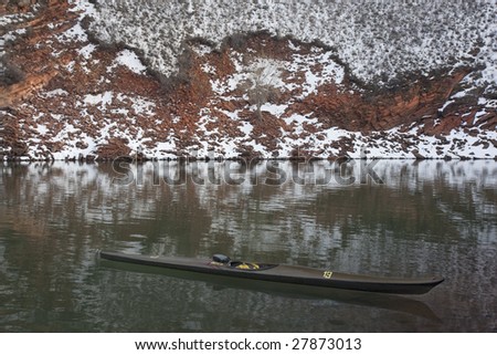 long, narrow, carbon fiber, racing sea kayak on mountain lake with high red sandstone cliffs covered by snow in  Colorado, thirteen - temporary race number placed on deck by myself