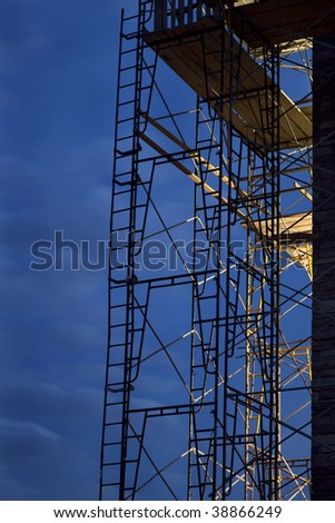 silhouette of construction scaffolding against nighttime sky with a strong light coming from building interior