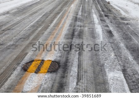 street asphalt pavement covered by snow and ice, double yellow line across manhole cover