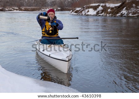 winter canoe paddling on icy river, taking a break for hot tea (South Platte River in eastern Colorado)