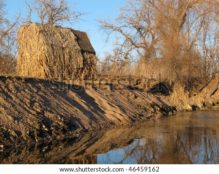 waterfowl hunting blind (shelter - plywood covered by straw) on river shore