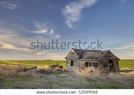old abandoned house and farming machinery on Colorado prairie with green fields in background